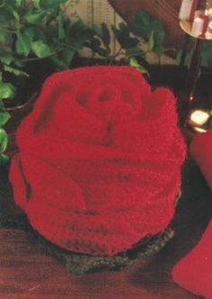 a red knitted rose sitting on top of a wooden table next to a plant