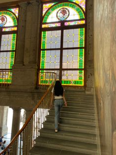 a woman walking up some stairs in front of stained glass windows