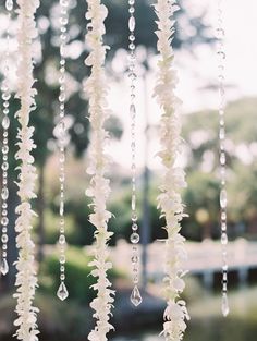 white flowers hanging from the ceiling in front of a building with trees and grass behind it