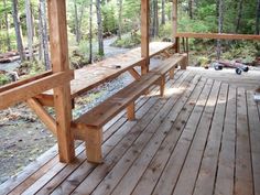 a wooden bench sitting on top of a wooden deck next to a forest filled with trees