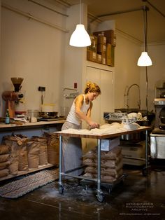 a woman working in a kitchen with lots of bags on the table and lights above her