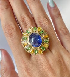 Dive into luxury with our Art Deco Vintage Natural Blue Sapphire Cocktail Ring, a tropical jungle-inspired masterpiece. The 11.4 carat oval cabochon-cut sapphire, resembling the azure waters of a hidden lagoon, takes center stage. Encircled by a lush arrangement of pear-cut yellow sapphires and tsavorites, evoking a vibrant foliage, while a dazzling melee of white sapphires ties it all together. This September birthstone beauty captures the essence of a tropical paradise on your finger. The Gold Luxury Multi-stone Sapphire Gemstones, Luxury Multicolor Sapphire Ring With Gemstone Accents, Luxury Multicolor Sapphire Ring, Luxury Sapphire Ring With Diamond Accents, Luxury Multicolor Emerald Gemstone Ring, Luxury Sapphire Gemstones With Accent Stones, Luxury Sapphire Gemstones With Gemstone Accents, Luxury Multi-stone Oval Sapphire Ring, Luxury Green Sapphire Jewelry