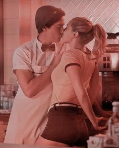 a man and woman kissing in front of a stove top oven while standing next to each other