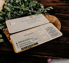 two metal business cards sitting on top of a wooden table next to flowers and greenery