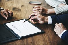 two people sitting at a table with a clipboard and pen in their hands, writing on the paper