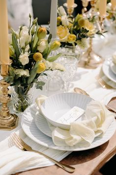 the table is set with white plates and yellow flowers