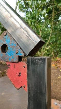 a metal object is sitting on top of a red and blue block in front of some trees