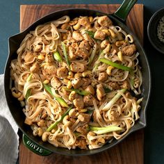 a skillet filled with noodles and meats on top of a wooden cutting board