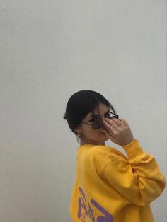 a woman in a yellow sweatshirt is holding her hand up to her face