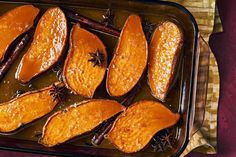 baked sweet potato wedges in brown gravy on a baking sheet with cinnamon sticks