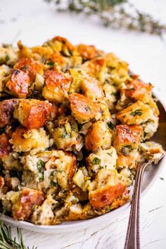 a white bowl filled with stuffing next to a spoon and sprig of rosemary