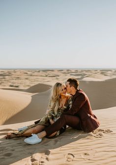 a man and woman sitting on top of a sandy beach next to the sand dunes