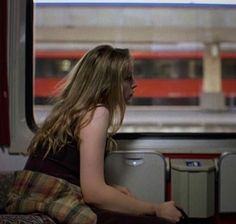 a woman sitting on a train looking out the window at another person in the distance