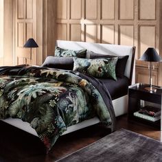 a bed covered in black and green comforter next to a night stand with two lamps