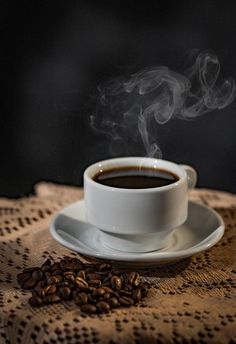 a cup of coffee sitting on top of a saucer next to some coffee beans