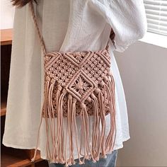 a woman wearing a white shirt holding a pink crocheted bag with tassels