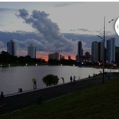 people are walking along the edge of a body of water at dusk with tall buildings in the background