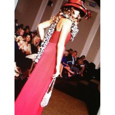 a woman in a long red dress and hat walking down the runway at a fashion show