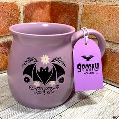 a purple mug with a bat on it and a tag hanging from the handle that says spooky hollowlow