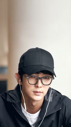 a young man wearing headphones and a black hat is looking at his cell phone