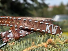 two brown leather belts with white stitching and monogrammed letters on them sitting in the grass