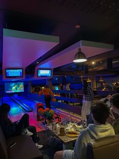 several people are bowling in a bowling alley at night time, with neon lights on the ceiling