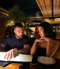 a man and woman sitting at a table with an open book in front of them