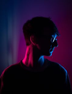 a man wearing glasses in the dark with red and blue light shining on his face