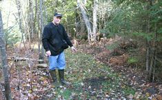 a man standing in the middle of a forest with lots of leaves on the ground