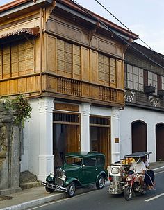 an old car parked in front of a building with wooden balconies on it