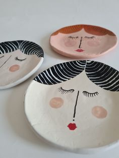 three plates with faces painted on them sitting on a white table top, one is pink and the other is black