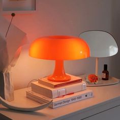 an orange lamp sitting on top of a white table next to books and a bottle