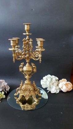 a gold candelabra with three candles on it and flowers in the background