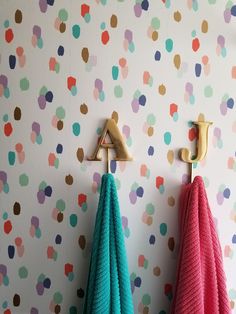 two colorful towels hanging on hooks in front of a wall with polka dot pattern paper