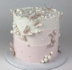 a pink and white wedding cake with butterflies on the top is decorated with pearls, icing and beads