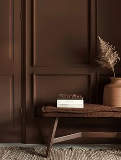 a table with a book, vase and plant on it in front of a brown wall