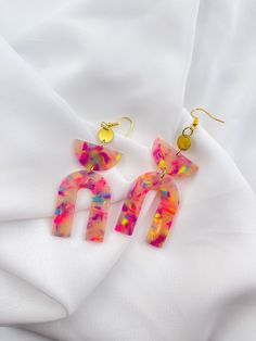 two pairs of pink and yellow acrylic earrings on top of a white sheet