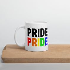 a white coffee mug with the words pride printed on it sitting on a wooden shelf