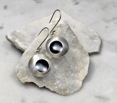 two silver spoons sitting on top of a rock next to a pair of earrings