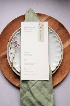 a place setting on a wooden plate with a green napkin and silverware, next to a white card