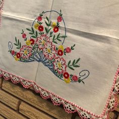 an embroidered table cloth with flowers on it sitting on top of a wooden bench next to a brick wall