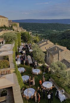 an aerial view of people standing around tables and umbrellas in the grass near some buildings