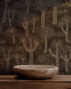 a bowl sitting on top of a wooden table in front of a wall with cactus designs