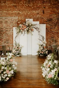 an indoor ceremony with flowers and greenery on the aisle, set up in front of a brick wall