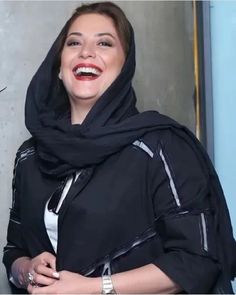 a woman wearing a black scarf and smiling at the camera with her hands in her pockets