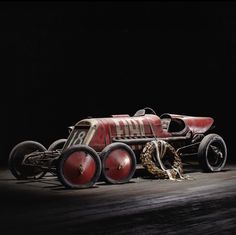 an old red race car sitting on top of a wooden floor next to a chain link fence