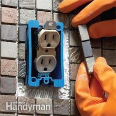 a person in orange gloves is working on an electrical outlet with a brick wall behind them