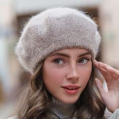 a woman wearing a knitted hat while holding her hand up to her ear