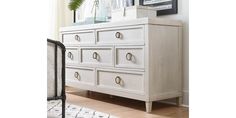 a white dresser sitting on top of a hard wood floor next to a rug and window