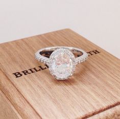 an oval shaped diamond ring on top of a wooden box with the word love written below it